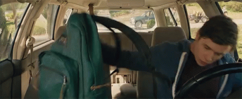 A Man Is Sitting In The Back Seat Of A Car With A Backpack On His Back . GIF