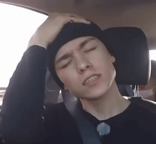 A Man Is Sitting In The Back Seat Of A Car With His Hand On His Head . GIF