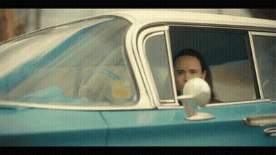 A Man Is Sitting In The Driver 'S Seat Of A Blue Car . GIF