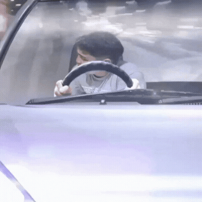 A Man Is Sitting In The Driver 'S Seat Of A Car Holding A Steering Wheel . GIF