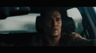 A Man Is Sitting In The Driver 'S Seat Of A Car Looking Out The Window . GIF