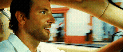 A Man Is Sitting In The Driver 'S Seat Of A Car While A Woman Holds His Hand Over His Head . GIF