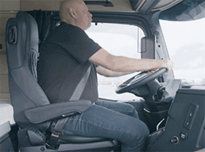 A Man Is Sitting In The Driver 'S Seat Of A Truck And Holding The Steering Wheel . GIF