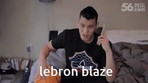 A Man Is Sitting On A Bed With A Basketball And The Word Lebron Blaze On His Shirt GIF