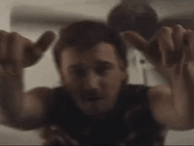 A Man Is Sitting On A Bed With His Arms Outstretched And Making A Hand Sign . GIF