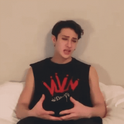 A Man Is Sitting On A Bed With His Hands On His Belly . GIF