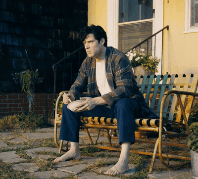 A Man Is Sitting On A Bench With A Bowl Of Food In His Hand GIF