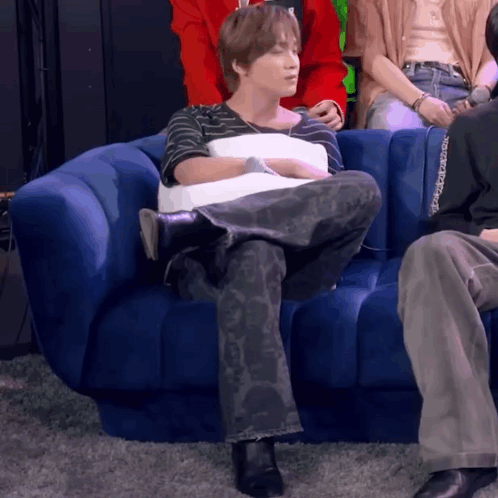 A Man Is Sitting On A Blue Couch Holding A Pillow . GIF