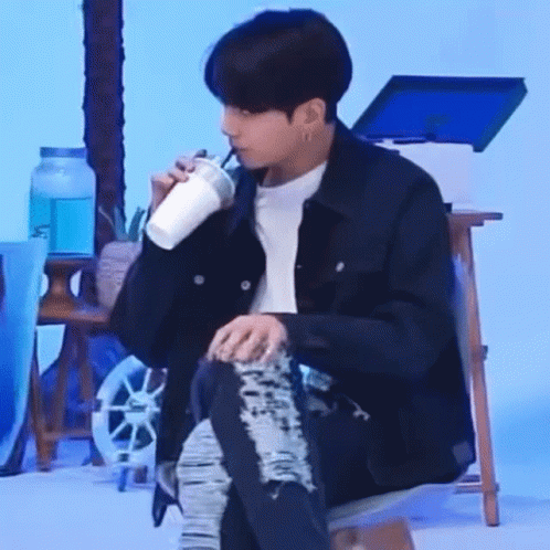 A Man Is Sitting On A Chair Drinking From A Cup . GIF
