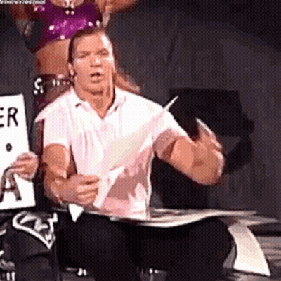 A Man Is Sitting On A Chair Holding A Piece Of Paper And A Woman Is Standing Behind Him . GIF
