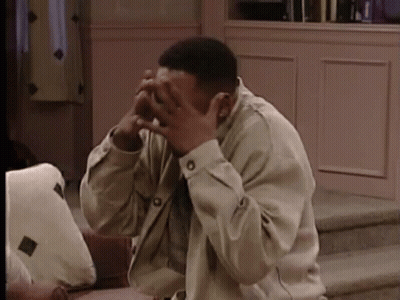 A Man Is Sitting On A Couch And Covering His Face With His Hands . GIF