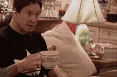 A Man Is Sitting On A Couch Drinking A Cup Of Tea . GIF