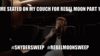 A Man Is Sitting On A Couch Drinking From A Cup In A Theater . GIF