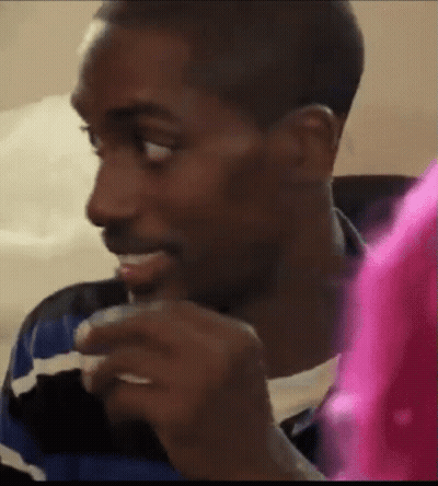 A Man Is Sitting On A Couch Eating A Sandwich While Looking At Something . GIF