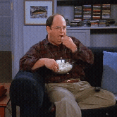 A Man Is Sitting On A Couch Eating Popcorn GIF