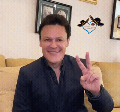 A Man Is Sitting On A Couch Giving The Peace Sign GIF