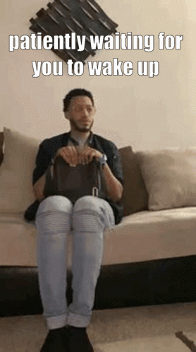 A Man Is Sitting On A Couch Holding A Bag And Waiting For Someone To Wake Up . GIF
