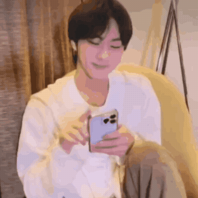 A Man Is Sitting On A Couch Holding A Cell Phone In His Hand . GIF