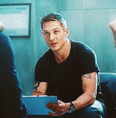 A Man Is Sitting On A Couch Holding A Clipboard And Looking At The Camera . GIF