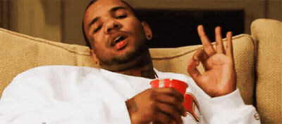 A Man Is Sitting On A Couch Holding A Cup Of Coffee And Making An Ok Sign . GIF