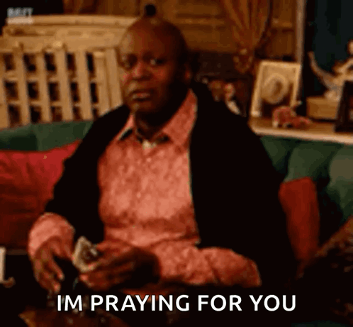 A Man Is Sitting On A Couch Holding A Glass Of Wine And Playing Cards And Saying `` Im Praying For You '' GIF