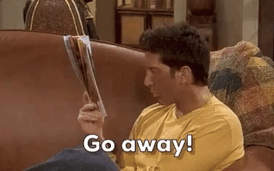 A Man Is Sitting On A Couch Holding A Magazine And Saying `` Go Away '' . GIF