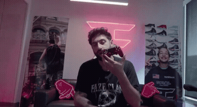A Man Is Sitting On A Couch Holding A Video Game Controller In His Hand . GIF
