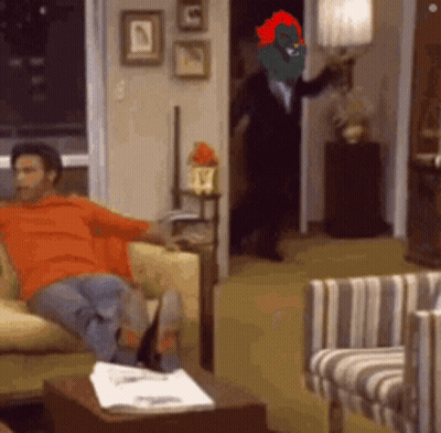 A Man Is Sitting On A Couch In A Living Room With A Cartoon Character On His Head GIF
