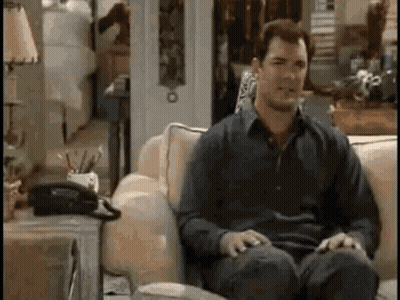 A Man Is Sitting On A Couch In A Living Room With A Telephone On The Table . GIF