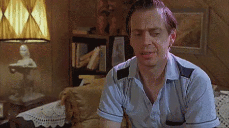 A Man Is Sitting On A Couch In A Living Room With His Eyes Closed And A Lamp In The Background . GIF
