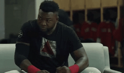 A Man Is Sitting On A Couch In A Locker Room Wearing A Black Shirt . GIF