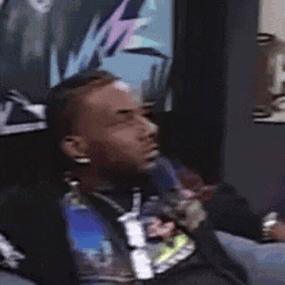 A Man Is Sitting On A Couch In Front Of A Wall With A Picture On It . GIF