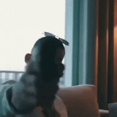 A Man Is Sitting On A Couch In Front Of A Window Wearing Sunglasses And A Mask . GIF