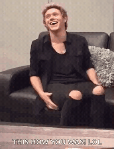 A Man Is Sitting On A Couch Laughing And Holding His Knee . GIF