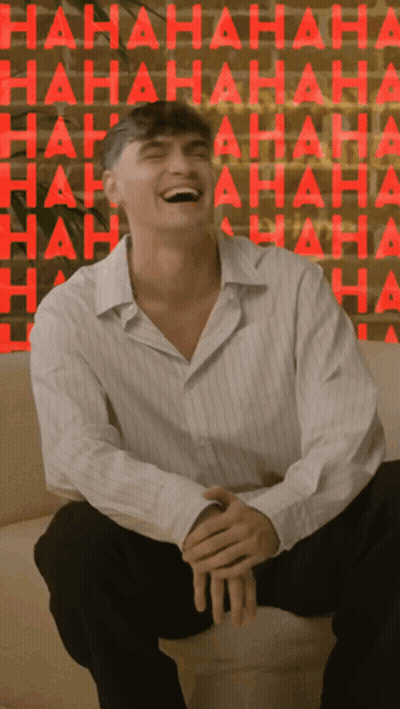 A Man Is Sitting On A Couch Laughing In Front Of A Wall That Says ' Hahaha ' GIF