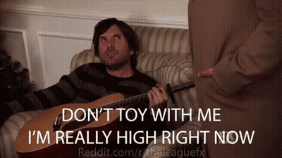 A Man Is Sitting On A Couch Playing A Guitar And Talking To Another Man GIF