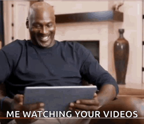 A Man Is Sitting On A Couch Watching A Video On A Tablet And Smiling . GIF