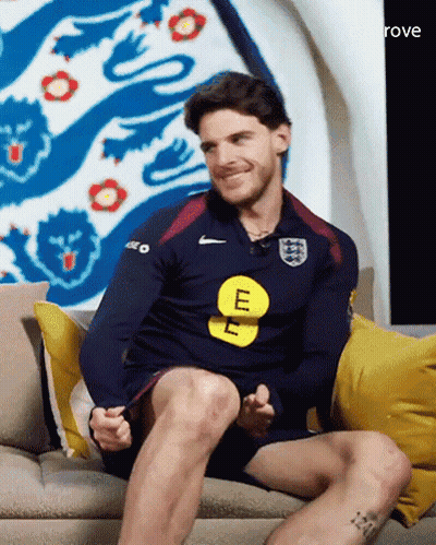 A Man Is Sitting On A Couch Wearing A Blue Nike Shirt With The Letter E On It GIF