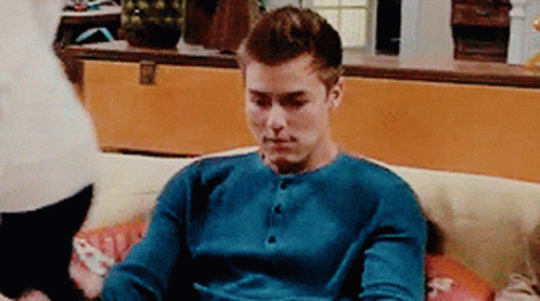A Man Is Sitting On A Couch Wearing A Blue Shirt GIF