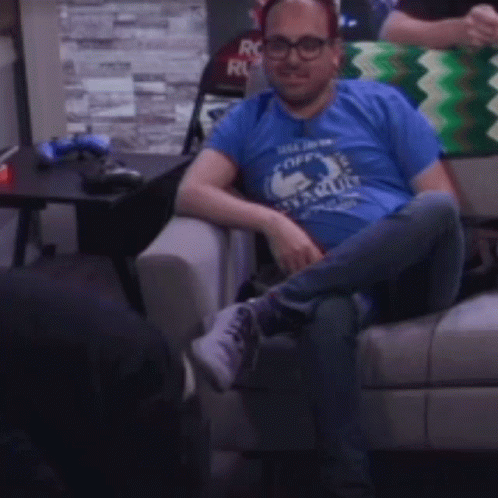 A Man Is Sitting On A Couch Wearing A Blue Shirt That Says " I Like Coffee " GIF