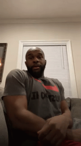 A Man Is Sitting On A Couch Wearing A Nike Shirt That Says Just Do It GIF