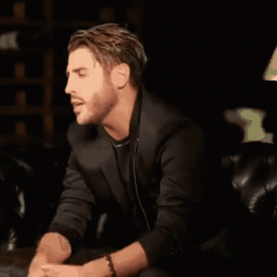 A Man Is Sitting On A Couch Wearing Headphones And A Black Jacket . GIF