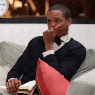 A Man Is Sitting On A Couch With A Book And A Pen In His Hand GIF