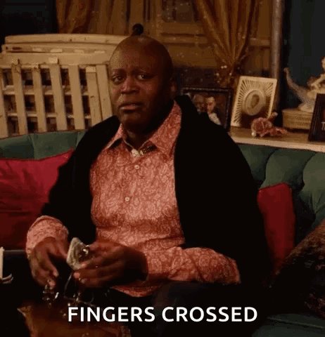 A Man Is Sitting On A Couch With A Glass Of Wine In His Hand And The Words Fingers Crossed Above Him . GIF