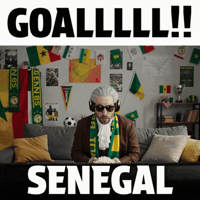 A Man Is Sitting On A Couch With A Scarf Around His Neck That Says Senegal GIF