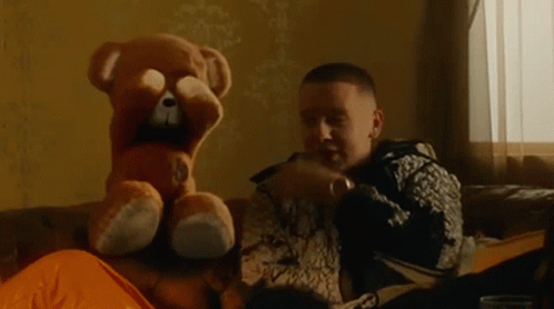 A Man Is Sitting On A Couch With A Teddy Bear Covering His Face . GIF