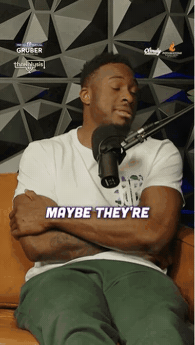 A Man Is Sitting On A Couch With His Arms Crossed And Says Maybe They 'Re In Front Of A Microphone GIF