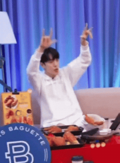 A Man Is Sitting On A Couch With His Arms In The Air And Making A Horn Sign . GIF