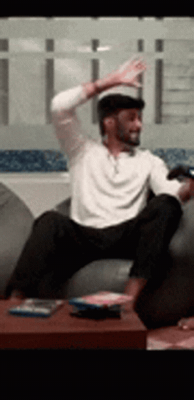 A Man Is Sitting On A Couch With His Arms In The Air . GIF