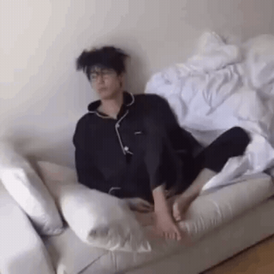 A Man Is Sitting On A Couch With His Feet Up And A Messy Haircut . GIF